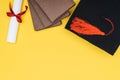 Top view of books, academic cap and diploma on yellow surface.