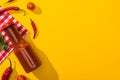 Top view of bottle with chili sauce, chili peppers and cilantro on yellow background