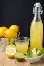 Top view of bottle with lemonade, glass, lemon wedges, lime, mint and whole lemons in metal bucket, on wooden table and black back Royalty Free Stock Photo