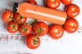 Top view of a bottle of tomato juice and fresh raw tomatoes on a white wooden background