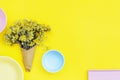 Top view of bouquet of dried yellow Helichrysum flowers in paper cornet and blue, yellow and lilac ceramic bowls on bright yellow