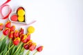 Top view on a bouquet of red-yellow tulips, a wooden box with macaroons and a red ribbon on a white background. Holiday card with Royalty Free Stock Photo