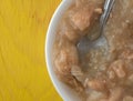 Top view of a bowl of canned chicken dumpling stew in a white bowl with a spoon atop a yellow table