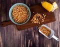 top view of bowl of corn seeds cut corn on cutting board with spoon full of corn seeds on wooden background