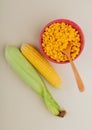 top view of bowl of corn seeds with wooden spoon and corn cobs on white background