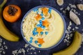 Top view of bowl filled with fruit and yoghurt smoothie decorated with pieces of banana and persimmon in shape of stars and moons