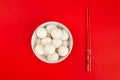 Top view of a bowl of glutinous rice balls with chopsticksisolated on a red background