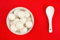 Top view of a bowl of glutinous rice balls with a spoon isolated on a red background