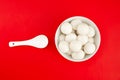 Top view of a bowl of glutinous rice balls with a spoon isolated on a red background