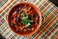 Top view of a bowl of homemade chilli topped with cilantro leaves on a colorful table mat