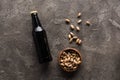 Top view of bowl with pistachios near bottle of dark beer on brown surface.
