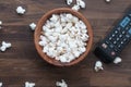 Top view of a bowl of popcorn and tv remote on table