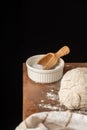 Top view of bowl with salt, pizza dough and kitchen towel, with selective focus, on wooden table with flour, black background,