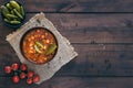 Top view of bowl with Solyanka, a spicy and sour soup of Russian origin, on dark wooden background with copy space