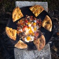 Top view of bread slices with vegetables and sausages frying with eggs in a pan on the fire