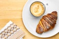 Top view on a breakfast consisting of a cup of coffee, a croissant on a wooden table with copy space. Serviette near the Royalty Free Stock Photo