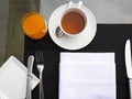 Top View of breakfast table, cup of hot tea, glass of orange juice, white napkin with tableware and eating utensils setting, fork Royalty Free Stock Photo