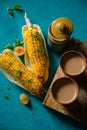 Indian Milk Tea served with roasted grilled corn on blue background. Two Delicious Grilled Corncobs and Two Cups of Chai.