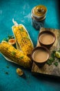 Steaming Hot Milk Tea served with roasted grilled corn on blue background. Two Delicious Grilled Corncobs and Two Cups of Chai.