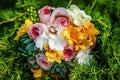 Top view of bridal bouquet with white, yellow and rose flowers with wedding rings on it lying on grass in summer wedding day. Royalty Free Stock Photo