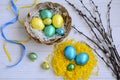Top view on bright blue, yellow and green Easter eggs in a wicker basket and a yellow decorative nest on a light wooden background