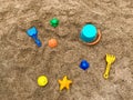 Top view of bright colored plastic molds, shovel, rake and bucket in the sandbox, against the background of dark sand with Royalty Free Stock Photo