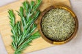 Top view of bright fresh green and dried rosemary branches, twigs and leaves in a wooden bowl and board on light background. Royalty Free Stock Photo