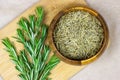 Top view of bright fresh green and dried rosemary branches, twigs and leaves in a wooden bowl and board on light background. Royalty Free Stock Photo