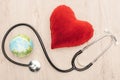 Top view of bright toy heart and toy earth, stethoscope on wooden background.