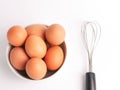 Top view a bunch of chicken eggs in a bowl with egg beater isolated on white background.