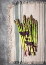 Top view of bundle of fresh green asparagus with purple basil leaves on a rustic line tablecloth.