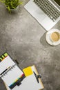 Top view of business desk with laptop, coffee, potted plant, notebook, notes paper and clipboard