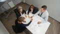 Top view of 4 business people sitting at a table and discussing blueprints. Designers engineers at a meeting.