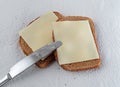 Top view of a butter knife atop two slices of wheat bread with margarine and cheese on paper towels