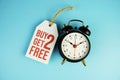 Buy two get two free text on tag sale with black alarm clock flat lay on blue background Royalty Free Stock Photo