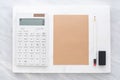 Top view of calculator, pencil, eraser and brown notepad on whi