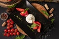 Top view Caprese salad. Mozzarella cheese, tomatoes and basil herb leaves on black plate over wood cuts, stone table in Royalty Free Stock Photo