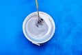 Top view captures process of stirring rod mixing fresh, white paint in bucket. Royalty Free Stock Photo