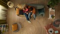 Top view capturing a young couple sitting on the couch together. The woman seems frustrated and her partner tries to