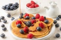 Top view of caramel falling on pancakes in plate with blueberries and raspberries with bowls and jar on white table Royalty Free Stock Photo