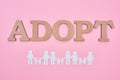 Top view of cardboard word adopt and paper cut families on pink background.