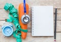 Top view carrot with blue stethoscope,measuring tape,alarm clock and notebook on wood table background