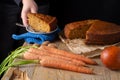 Top view of carrots, walnuts, orange, woman`s hand depositing portion on wooden table and carrot cake, with black background,