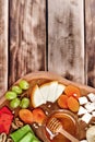 Top view of cheese plate - various types of cheese, honey, grapes, dried apricots, nuts and figs on a wooden board.