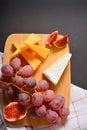 Top view of Cheeseboard platter with hard and soft mould cheese, grape and segmented fig on wooden board