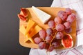 Top view of Cheeseboard platter with hard and soft mould cheese, grape and segmented fig on wooden board