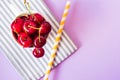 Top view of cherries on a stripped cloth and a yellow stripped straw on purple background Royalty Free Stock Photo