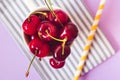 Top view of cherries on a stripped cloth and a yellow stripped straw and flower on purple or pink background Royalty Free Stock Photo