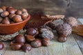 Top view of chestnuts with leaves and ceramic bowl with hazelnuts in the background, on weathered wooden background Royalty Free Stock Photo