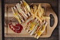 Top view of chicken club sandwiches and french fries on rustic wooden table